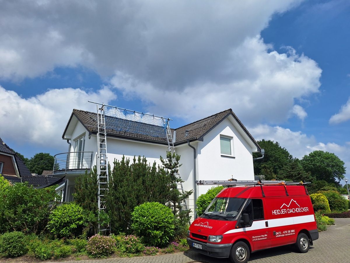 Ein weißes Haus mit einer Dachleiter und einem Wartungsnetz, daneben ein roter Lieferwagen unter einem bewölkten Himmel.